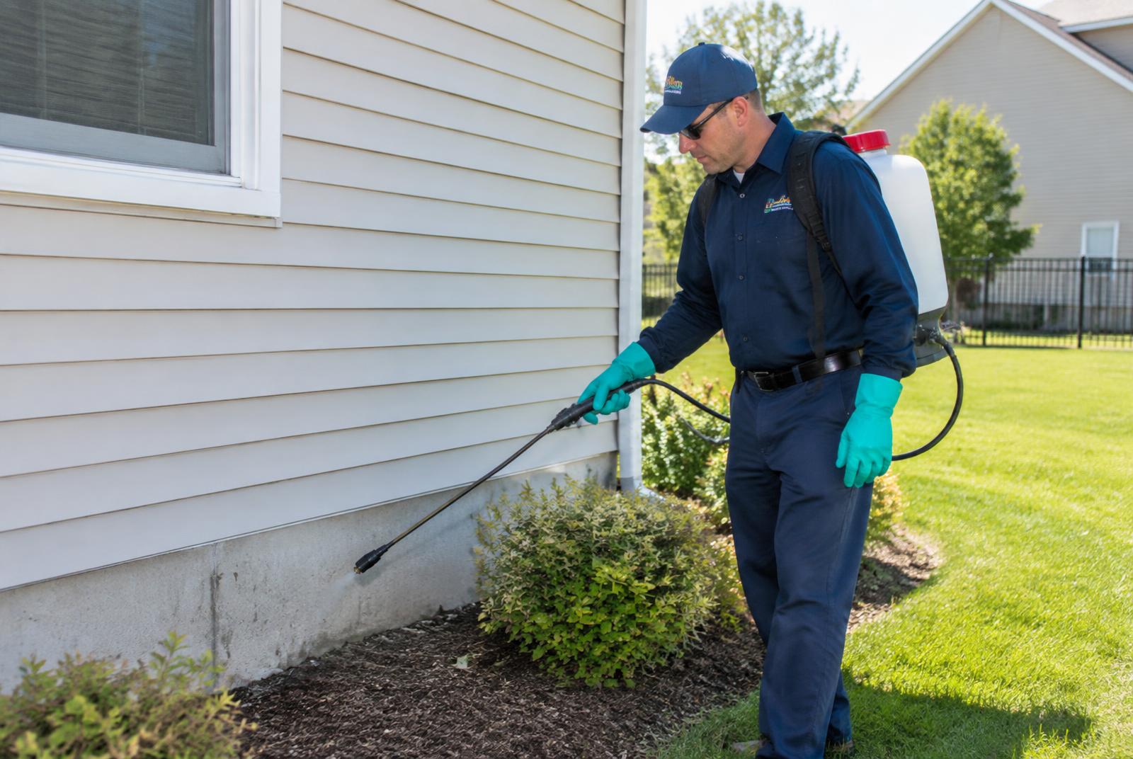 Pest control technician spraying a perimeter treatment along the foundation of a home in Anderson, Indiana